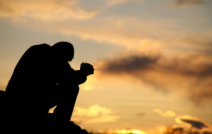 A silhouette of a man praying at sunset
